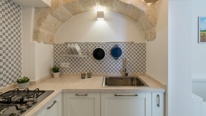 A kitchen with a stone arch, white cabinets, a stainless steel sink, and patterned backsplash tiles. - Casetta Biancapietra by Wonderful Italy (Ostuni)