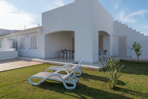 Un edificio moderno blanco con un patio cubierto, asientos al aire libre y un pequeño jardín.