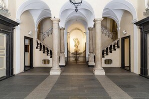 A grand hallway with a central statue, flanked by columns and arches, leading to a staircase. - Casa Giustiniani by Wonderful Italy (Genoa)