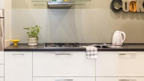 A modern kitchen with white cabinets, a stainless steel range hood, a glass shelf with decorative items, and a kettle on the counter. - Casa Roma al Centro di Palermo by Wonderful Italy (Palermo)