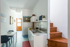 Une cuisine moderne avec un plan de travail blanc, un évier en acier inoxydable et un escalier en bois.