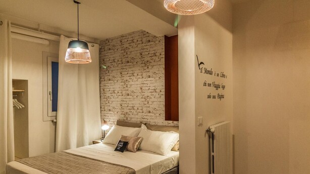 A bedroom with a brick-patterned wall, a bed with a geometric-patterned bedspread, a bedside lamp, and a wall-mounted radiator. - Corte Galluzzi in Basilica by Wonderful Italy (Bologna)