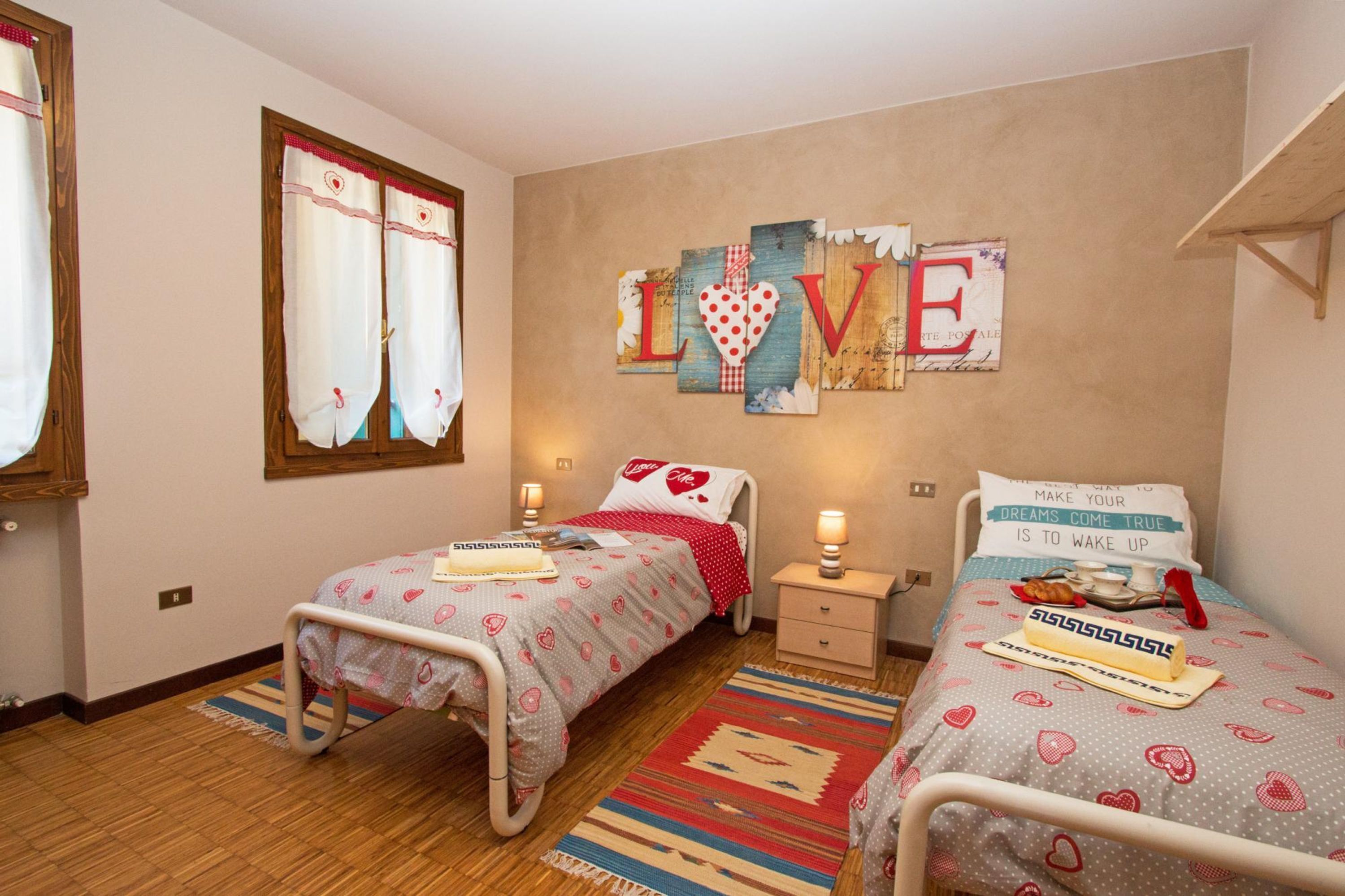 A bedroom with two single beds, a wall decoration spelling "LOVE", and a bedside table with a lamp.
