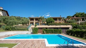 A large rectangular swimming pool with a wooden deck in the foreground, surrounded by well-maintained lawns and greenery. - Crocus 1 con Piscina by Wonderful Italy (Soiano del Lago)
