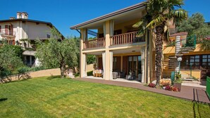 A two-story house with a balcony, a lawn, and a palm tree. - Crocus 1 con Piscina by Wonderful Italy (Soiano del Lago)
