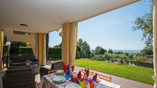 A dining area with a table set for four, overlooking a lush garden and a body of water. - Crocus 1 con Piscina by Wonderful Italy (Soiano del Lago)