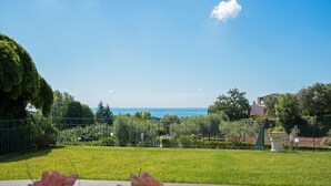 A view of a well-maintained garden with a wooden deck in the foreground, a metal fence, and a clear blue sky. - Crocus 1 con Piscina by Wonderful Italy (Soiano del Lago)