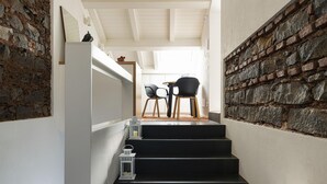 Een trap leidt naar een eetruimte met een stenen muur, zwarte stoelen en een witte tafel.