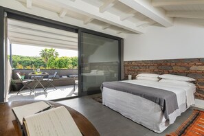 Een slaapkamer met een groot bed, een accentmuur van steen en een schuifdeur naar een terras met uitzicht op groen.