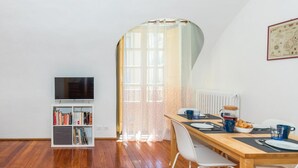 Ein Essbereich mit einem Holztisch, weißen Stühlen und einem Fernseher auf einem Regal.