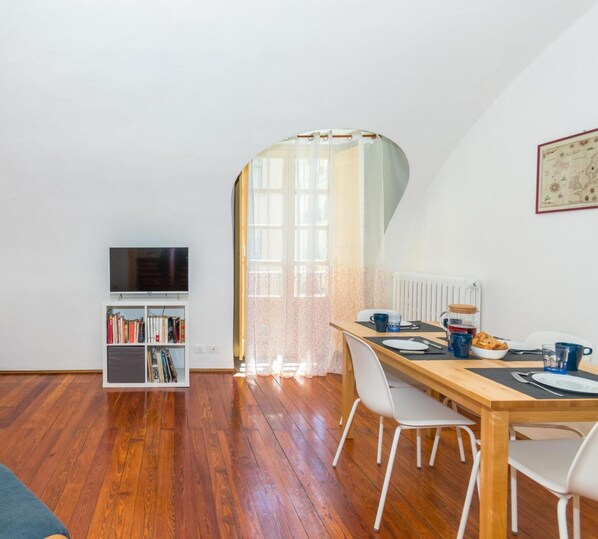A dining area with a wooden table, white chairs, and a television on a shelf. - San Carlo Apartment by Wonderful Italy (Turin)
