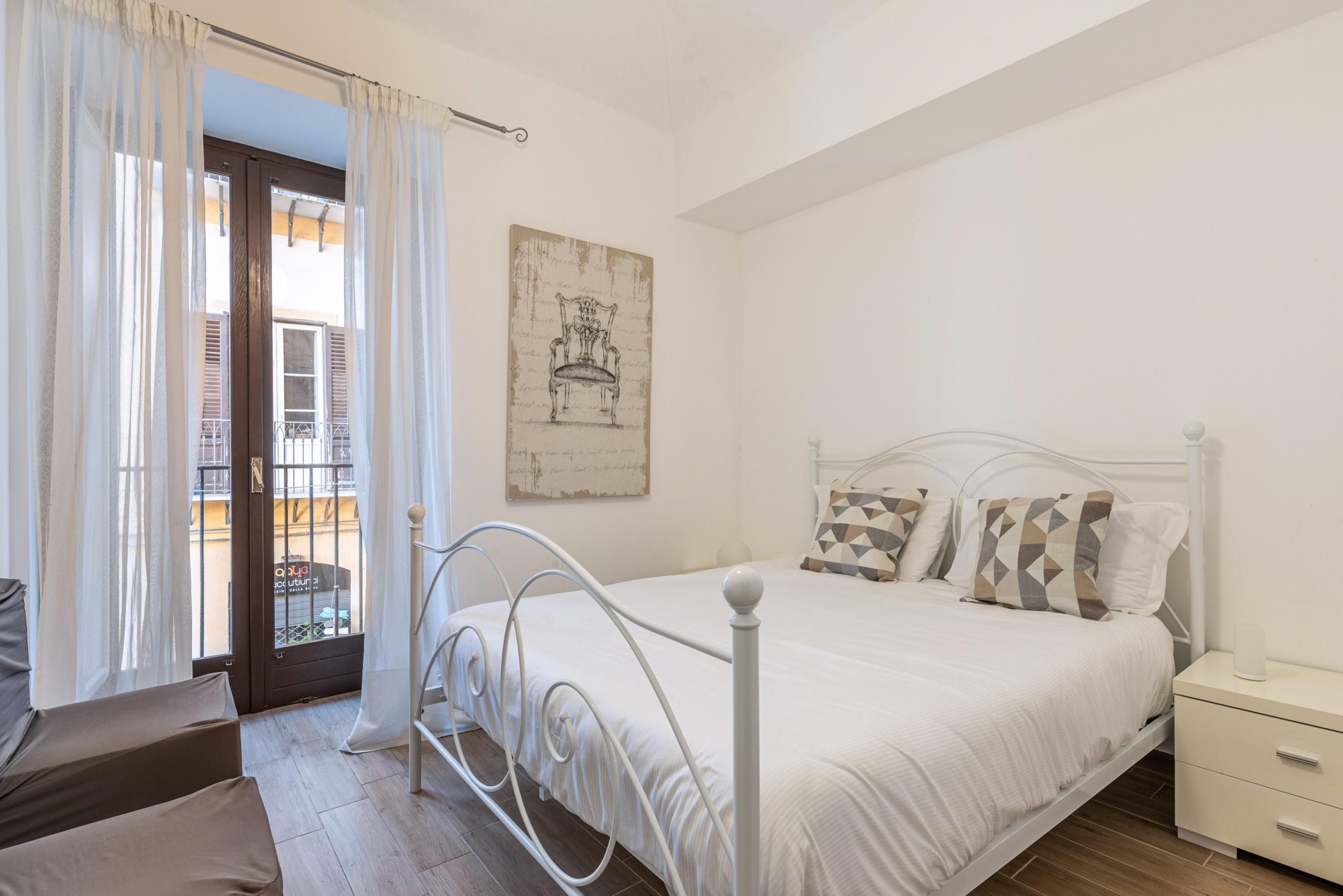 A bedroom with a bed, a nightstand, a window with curtains, and a door leading to a balcony.