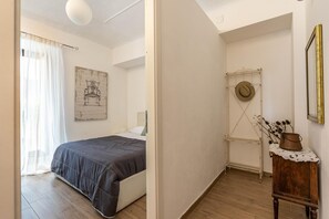 Ein Schlafzimmer mit einem Bett, einem Sessel, einem Wandhaken für Hüte, einem Holzschrank und einem gerahmten Bild.
