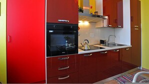 Eine kleine Küche mit roten Schränken, einem schwarzen Backofen und einer Edelstahl-Spüle.
