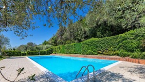 A rectangular swimming pool with a tiled deck, surrounded by lush greenery and a brick wall. - Residence San Giorgio PT 3 by Wonderful Italy (Toscolano Maderno)