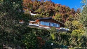A modern house with a flat roof, large windows, and a balcony, surrounded by lush greenery and trees. - Residence San Giorgio PT 3 by Wonderful Italy (Toscolano Maderno)