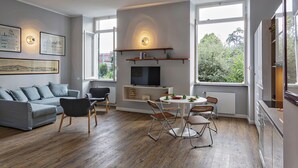 A modern living room with a grey sofa, a dining table with chairs, a TV on a shelf, and large windows offering a view of greenery. - Modern Loft in the Center by Wonderful Italy (Genoa)