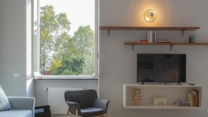 A modern living room with a large window, a flat-screen TV, and built-in shelves with books and decorative items. - Modern Loft in the Center by Wonderful Italy (Genoa)