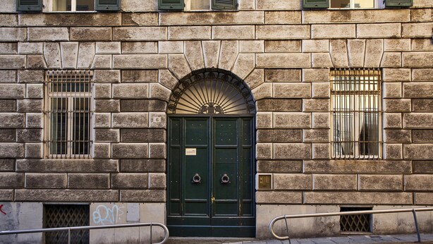A stone building with a green double door, two barred windows, and a metal railing in front. - Modern Loft in the Center by Wonderful Italy (Genoa)