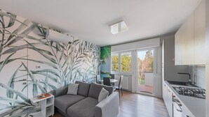 A modern living room with a grey sofa, a white side table, and a kitchen area with a stove. - Maisonnette Il Todeschino B12 by Wonderful Italy (Sirmione)