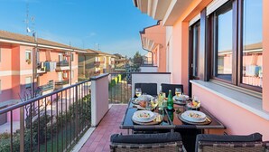 A balcony with a dining table set for two, overlooking a row of pink buildings. - Maisonnette Il Todeschino B12 by Wonderful Italy (Sirmione)