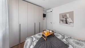 A bedroom with a bed, a wardrobe, a bedside table with a tray, and a wall-mounted TV. - Maisonnette Il Todeschino B12 by Wonderful Italy (Sirmione)