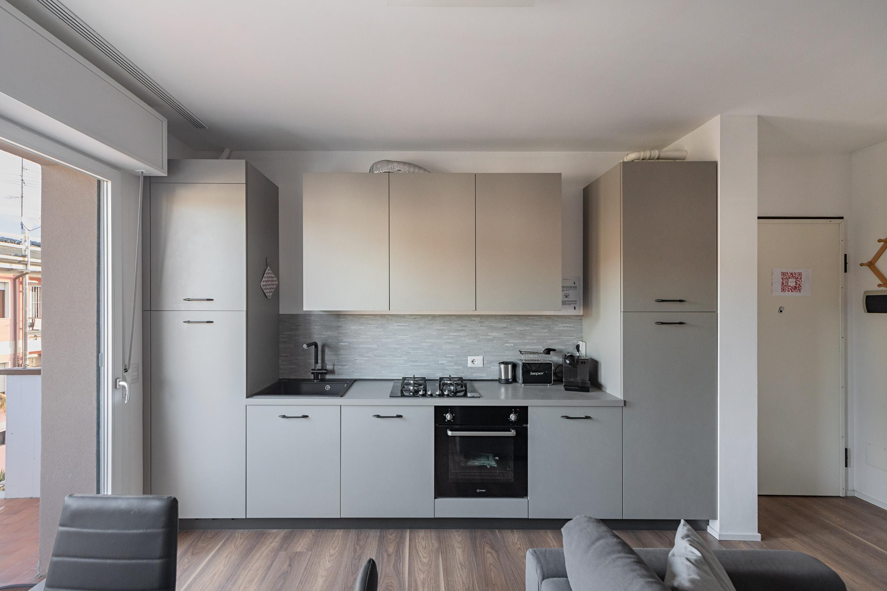 Eine moderne Küche mit grauen Schränken, einem eingebauten Backofen und einer Arbeitsplatte mit Wasserkocher und Toaster.