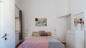 Une chambre à coucher avec un lit, une commode, un tableau accroché au mur et une porte.