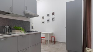 Une cuisine moderne avec des meubles gris, une cuisinière à gaz, une bouilloire et une petite table avec des chaises rouges.