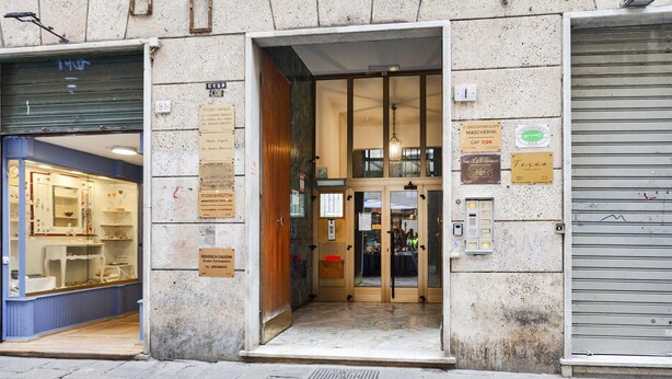 A building entrance with multiple business signs, a visible door, and a tiled pavement. - Marvelous Soziglia Apartment by Wonderful Italy (Genoa)