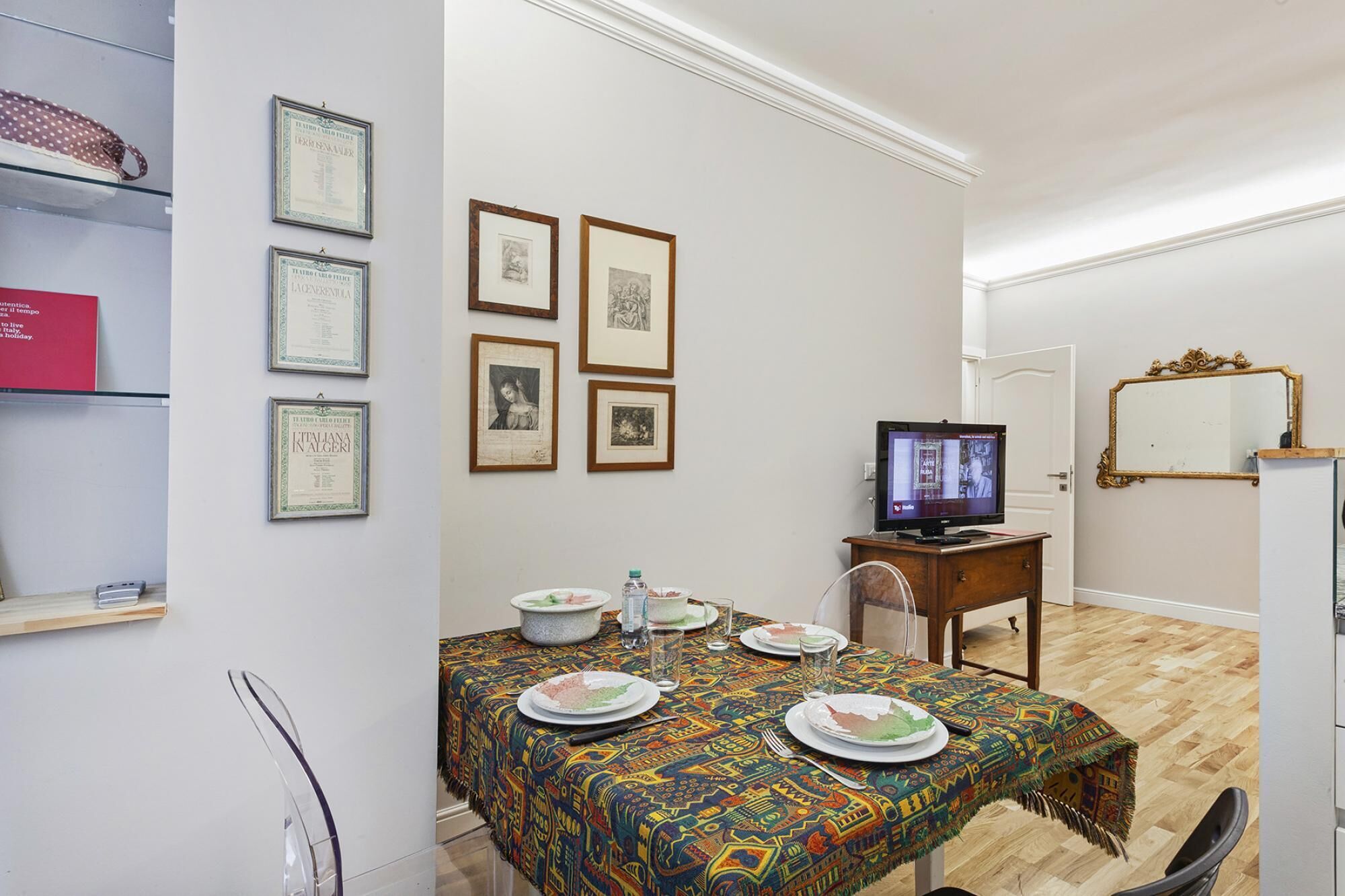 A small, furnished room with a dining table set for two, a television, and framed certificates on the wall.