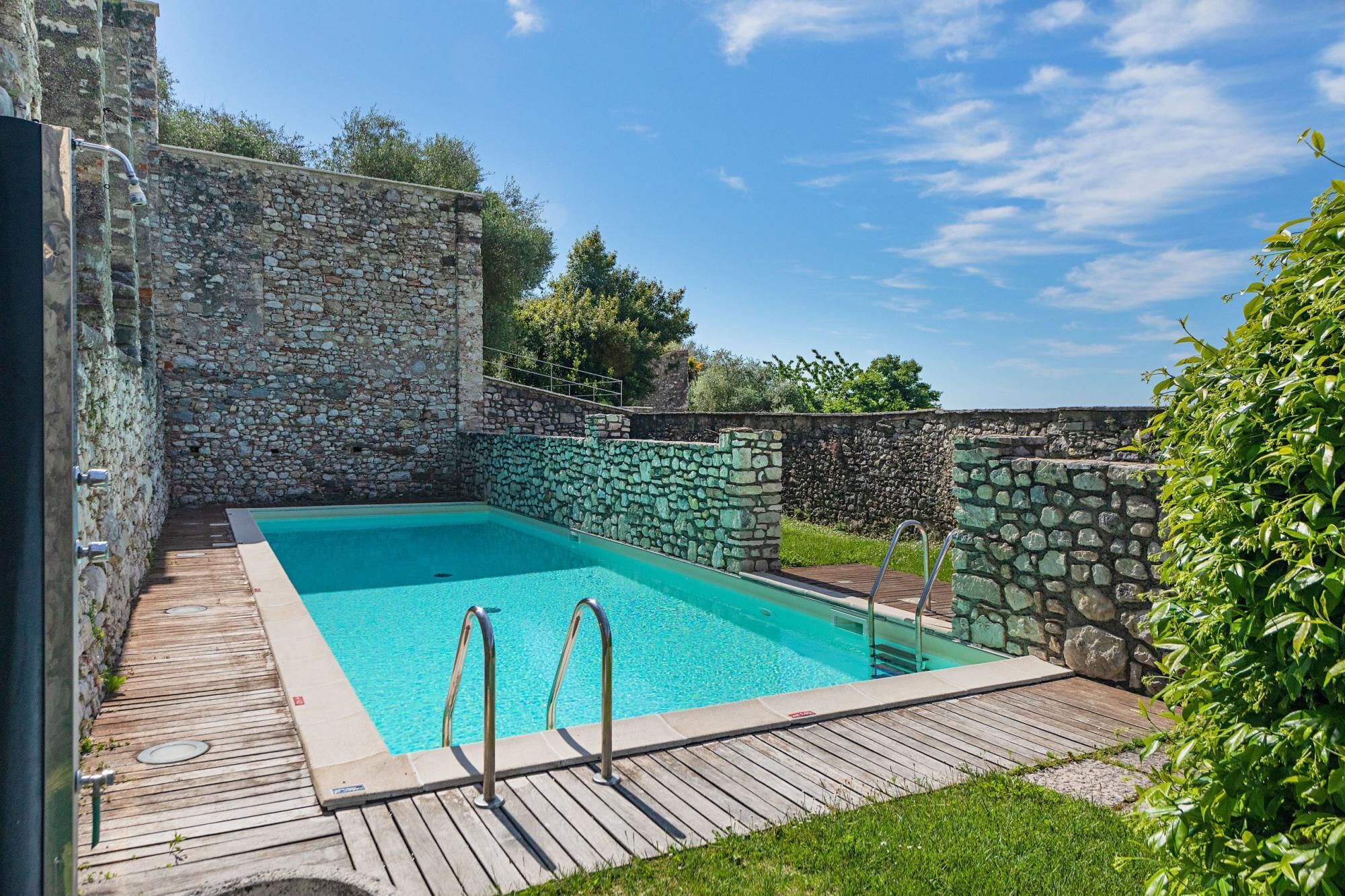 Una piscina rettangolare con pareti in pietra e un solarium in legno.