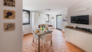 A modern kitchen with a dining area, white cabinetry, a television mounted on the wall, and a tiled floor. - Lemon House 2 Apartment by Wonderful Italy (Gardone Riviera)