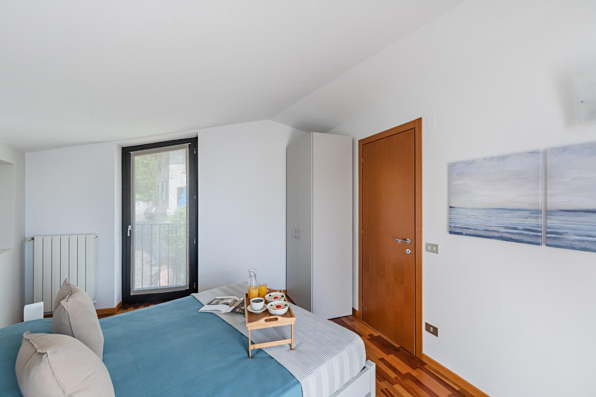 Ein Schlafzimmer mit einem Bett, einer Holztür, einem Fenster und einem Bild an der Wand.