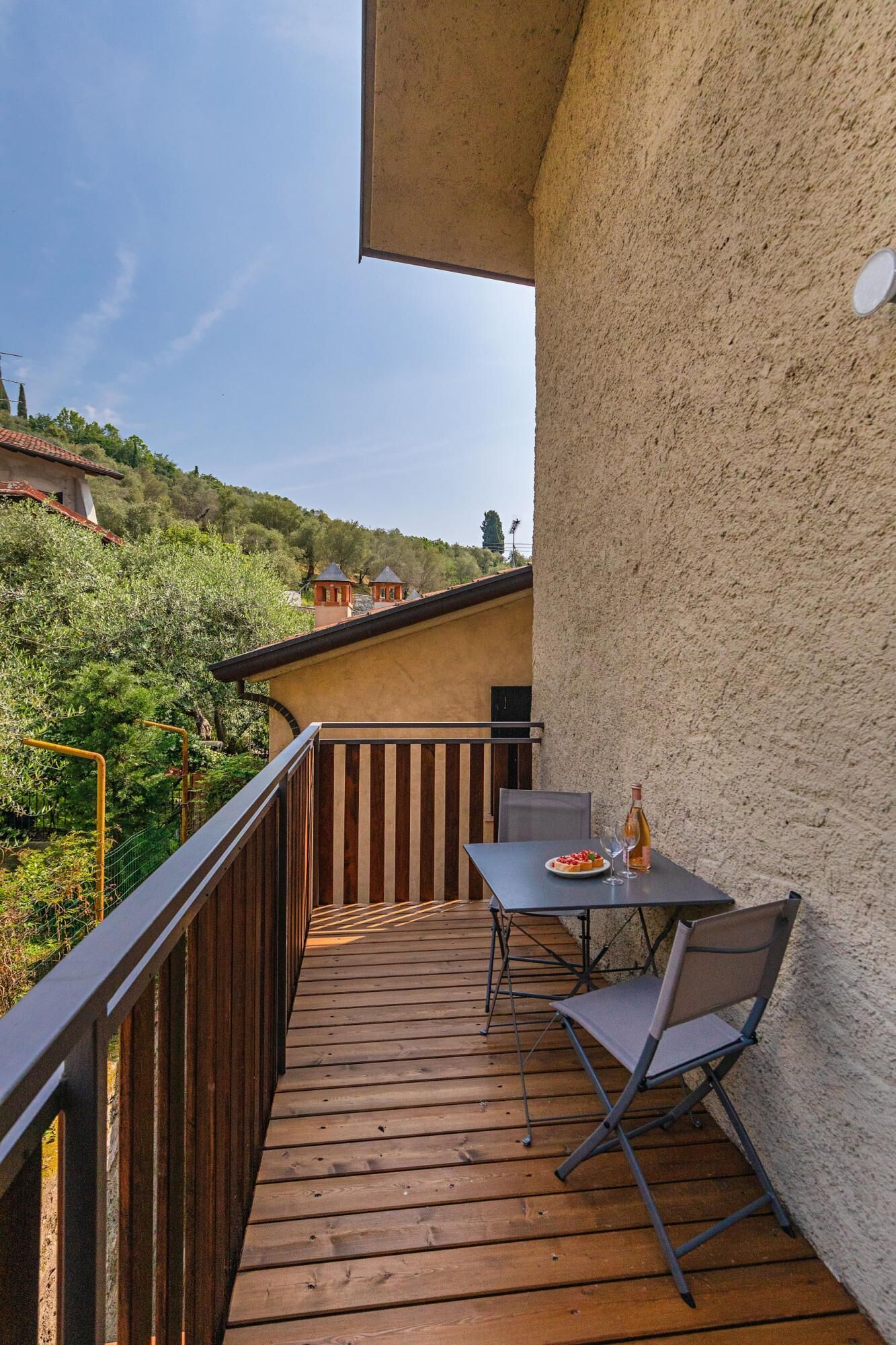 A wooden deck with a table and chairs, overlooking a hillside with buildings.