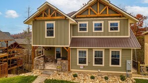 A two-story house with a stone foundation, a wooden deck, and a stone pathway leading to the entrance. - Harmony Peak (Gatlinburg)