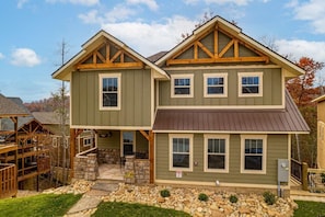 A two-story house with a stone foundation, a wooden deck, and a stone pathway leading to the entrance.