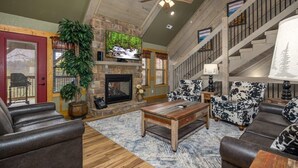 A spacious living room with a stone fireplace, wooden ceiling, and a large TV. - Harmony Peak (Gatlinburg)
