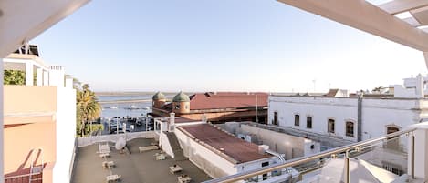 A rooftop terrace with a view of the sea, a building with domed roofs, and a white building with a red roof.