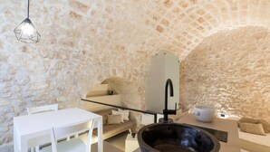 A stone-walled room with a white table and chairs, a large stone basin, and a modern light fixture.