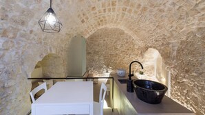 A stone-walled kitchen with a white table and chairs, a hanging light fixture, and a black sink.