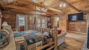 Una camera in legno tipica delle case di tronchi, con un letto, una televisione, pareti in legno e una ventola a soffitto.