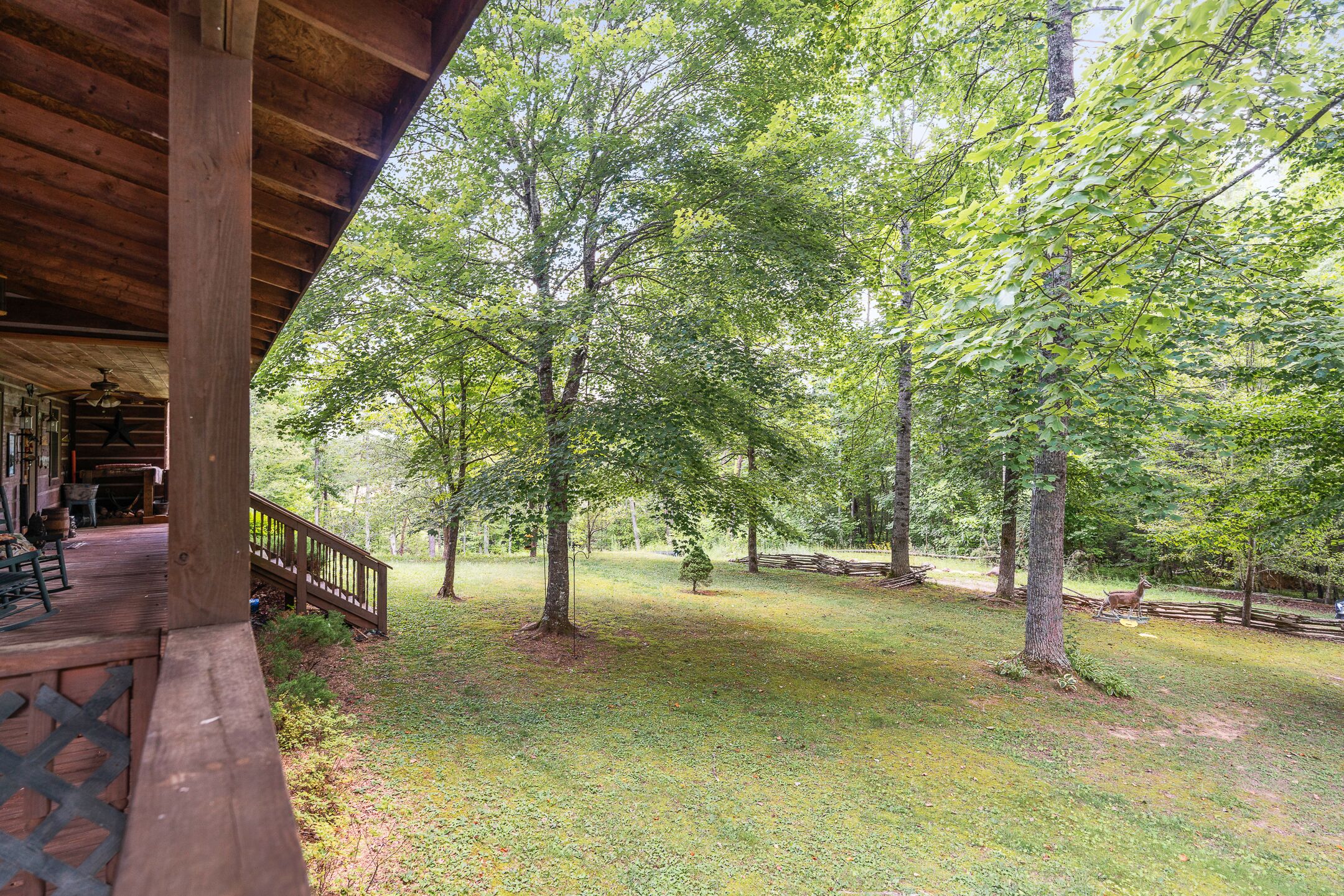 A wooden deck with a railing, surrounded by trees and a grassy area.
