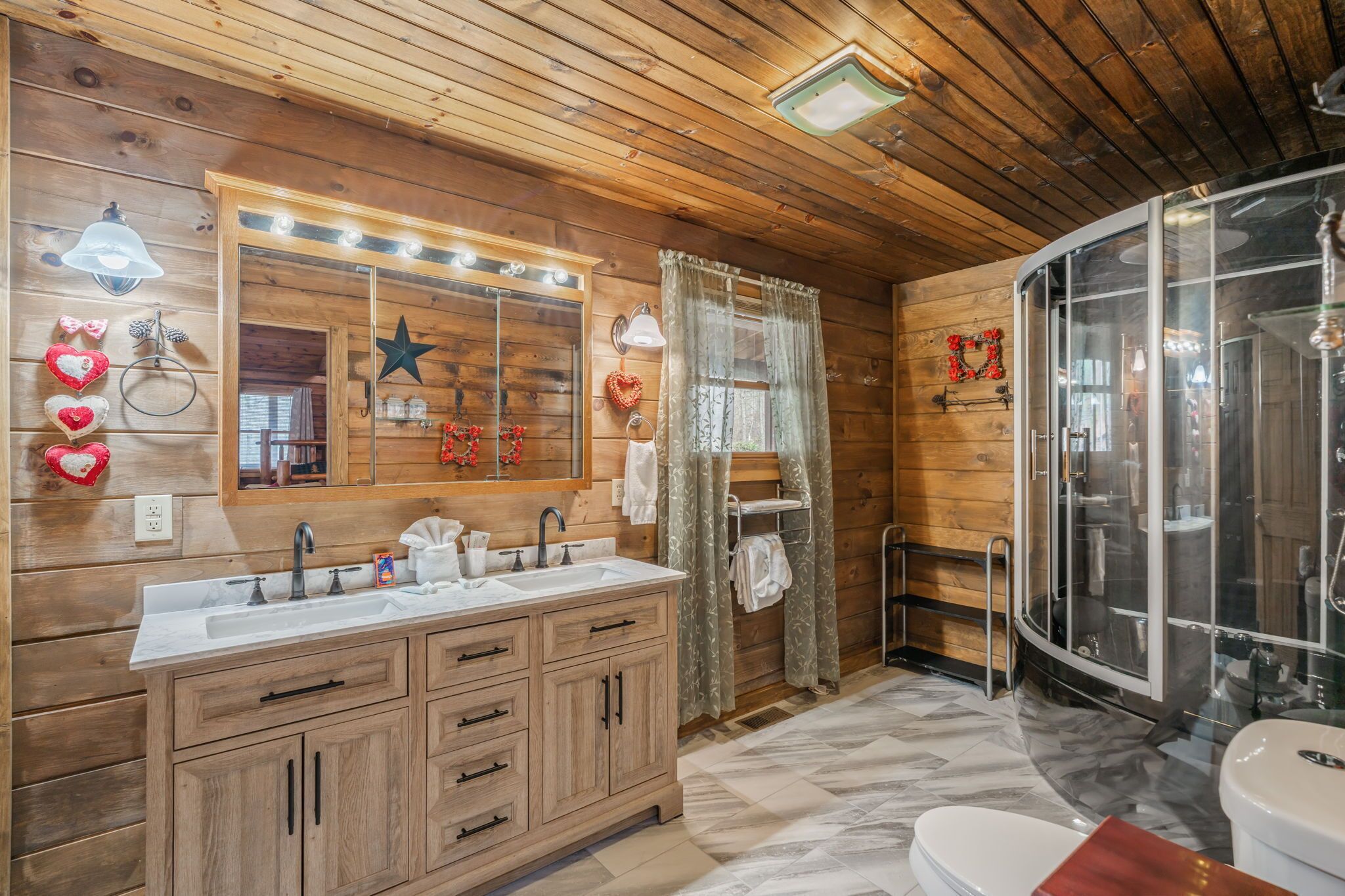 A wooden cabin-style bathroom with a vanity, mirror, shower, and a star decoration on the wall.