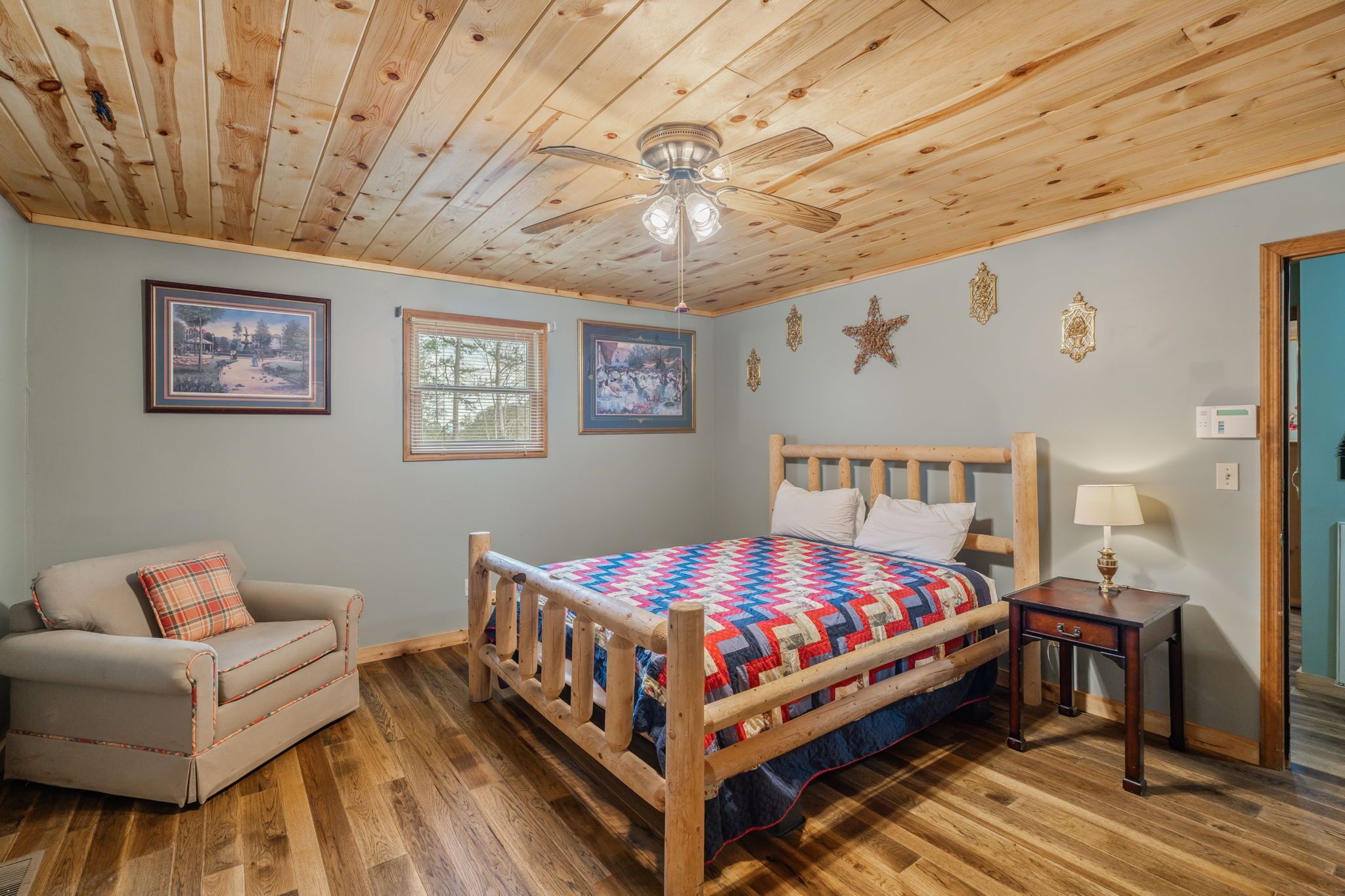 A bedroom with a wooden ceiling, a bed with a colorful quilt, a wooden nightstand, and a chair.