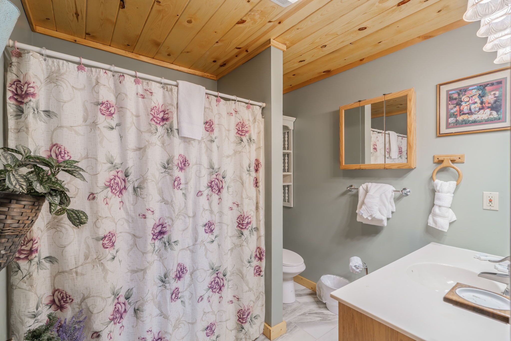 A bathroom with a shower curtain, toilet, sink, and wooden ceiling.