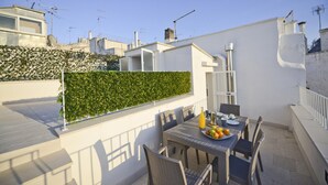 A rooftop terrace with a dining table set for two, surrounded by chairs, and a green hedge wall. - Scirocco Apartment With Terrace by Wonderful Italy (Ostuni)