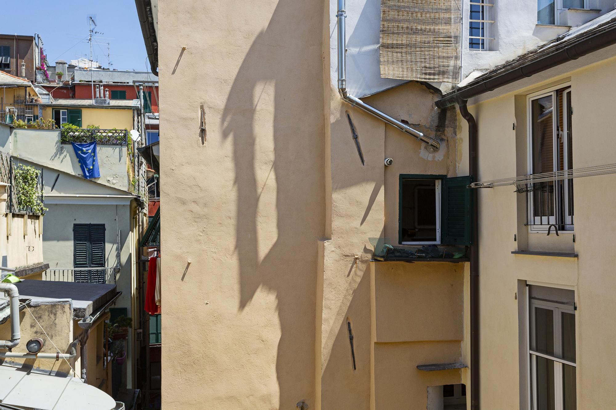 A narrow alleyway between buildings with a beige wall on the left and a yellow building on the right.