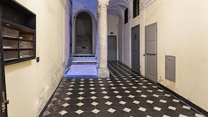 Um corredor com piso xadrez, portas em arco e escada que leva a um andar superior.