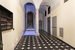 Un pasillo con piso a cuadros, arcos y una escalera que sube a un nivel superior.